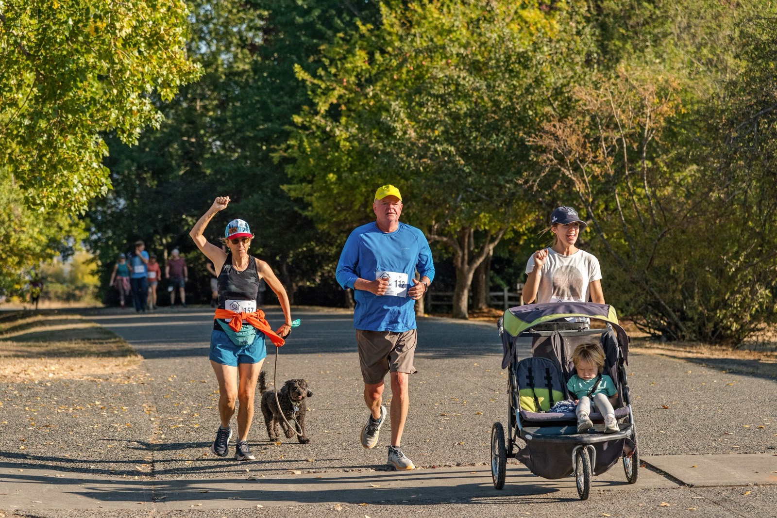 Adults running a park path together, one pushing a child in a buggy.