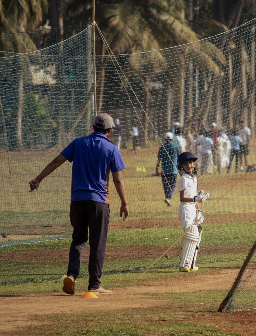 A coach and a young batsman at cricket nets on a public ground in Mumbai.